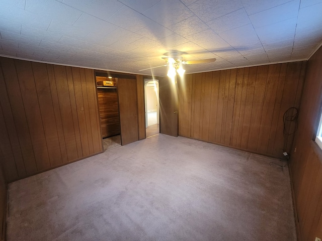 carpeted spare room with wood walls and ceiling fan