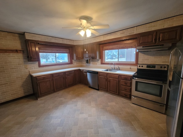 kitchen with sink, stainless steel appliances, a healthy amount of sunlight, and brick wall