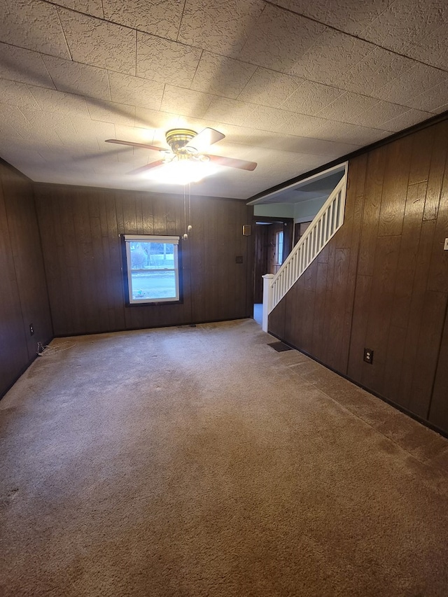 carpeted spare room featuring wood walls and ceiling fan