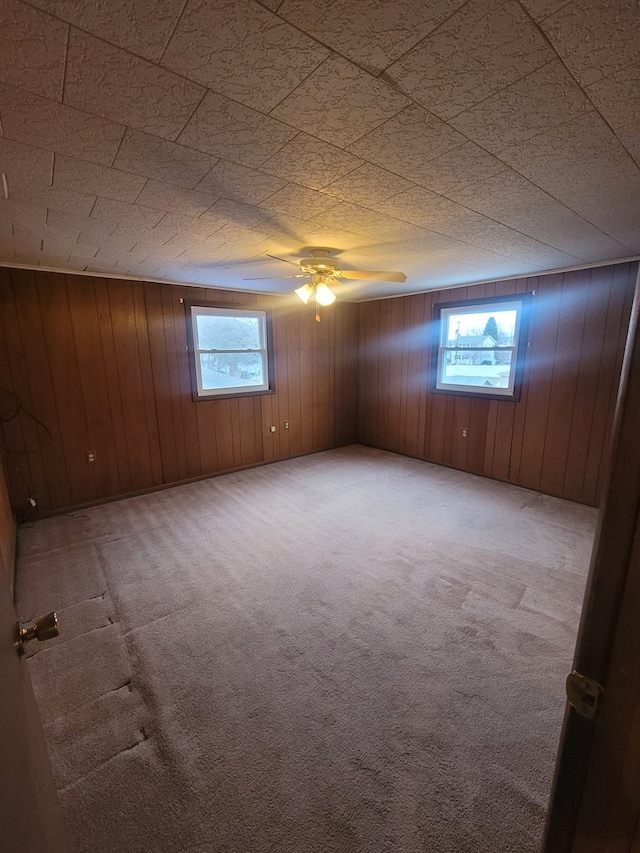 carpeted spare room with ceiling fan and wood walls