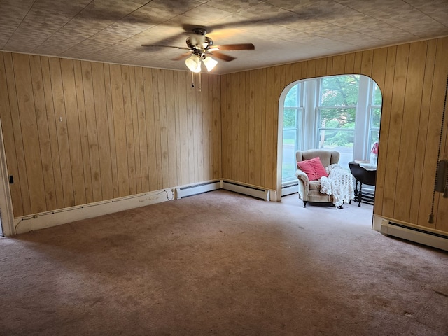 unfurnished room featuring carpet flooring, wood walls, ceiling fan, and baseboard heating