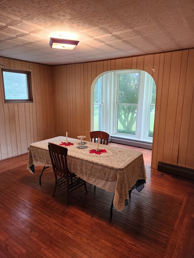 dining room with dark hardwood / wood-style flooring, a baseboard heating unit, and wood walls