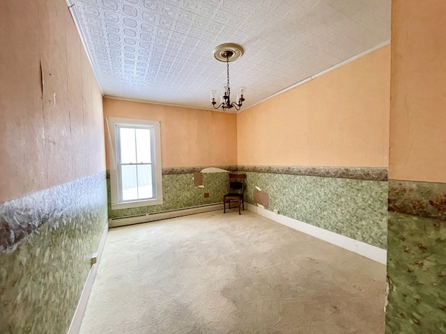 spare room featuring baseboard heating, carpet, ornamental molding, and an inviting chandelier