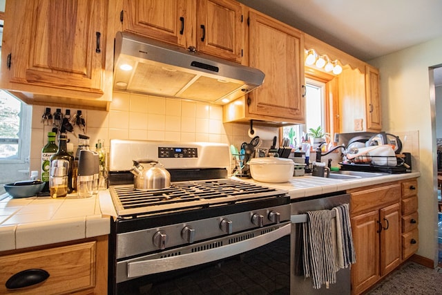 kitchen with stainless steel range, backsplash, tile countertops, and sink