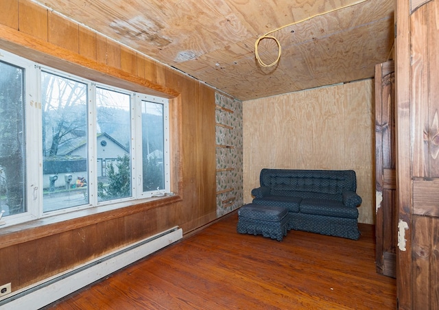 unfurnished room featuring wooden ceiling, a baseboard heating unit, wooden walls, hardwood / wood-style flooring, and a healthy amount of sunlight