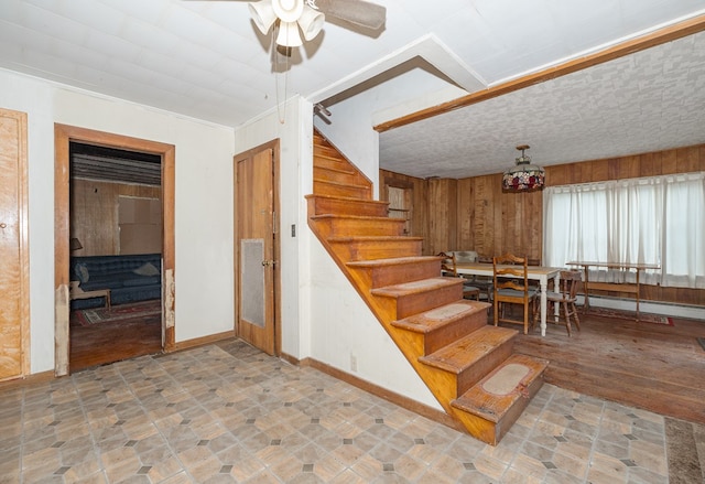 stairs featuring wooden walls, crown molding, ceiling fan, and a baseboard heating unit