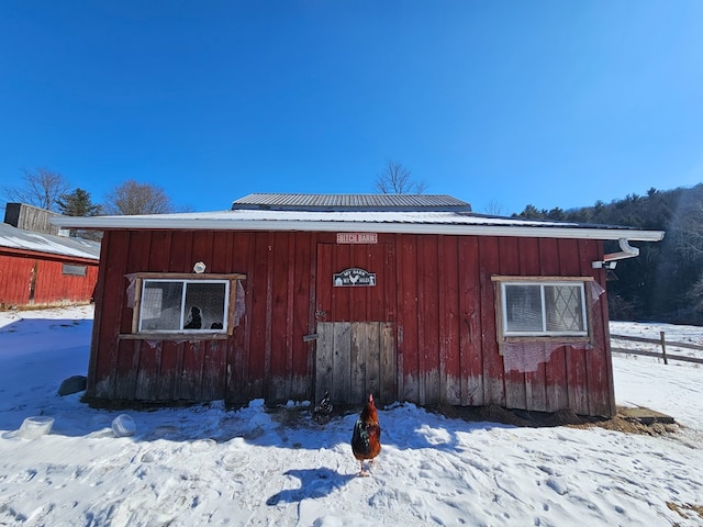 view of snow covered exterior featuring board and batten siding, an outbuilding, and metal roof