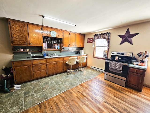 kitchen with brown cabinets, built in desk, light wood-style flooring, baseboard heating, and stainless steel range with electric stovetop