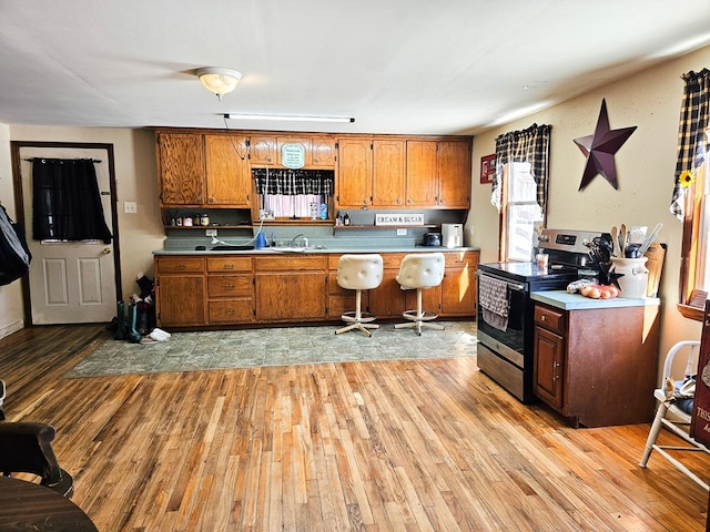 kitchen featuring light wood-style floors, stainless steel electric range, brown cabinets, and light countertops