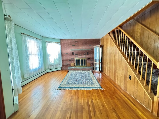 unfurnished living room with light hardwood / wood-style flooring, a baseboard radiator, a brick fireplace, and wood walls