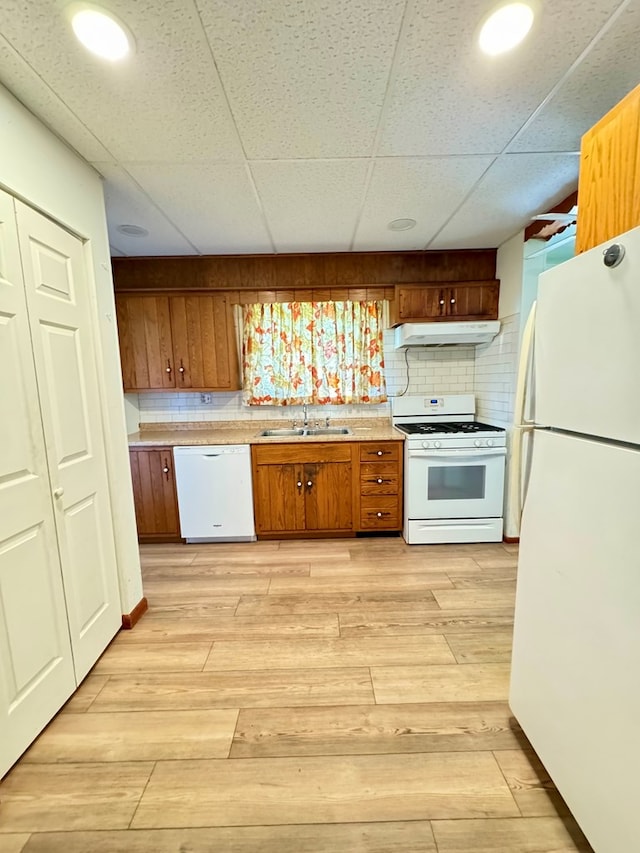 kitchen with decorative backsplash, light wood-type flooring, a paneled ceiling, white appliances, and sink