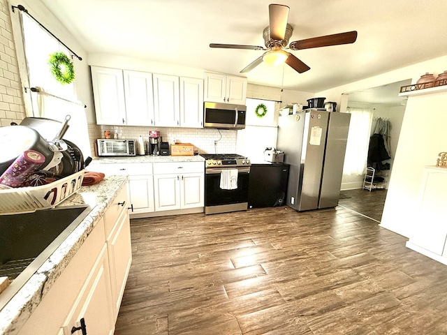 kitchen featuring white cabinets, decorative backsplash, ceiling fan, appliances with stainless steel finishes, and dark hardwood / wood-style flooring