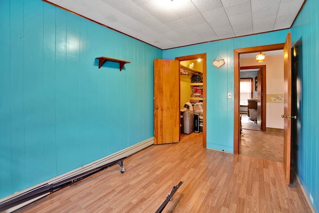 unfurnished bedroom with a walk in closet, baseboard heating, a closet, and light hardwood / wood-style floors