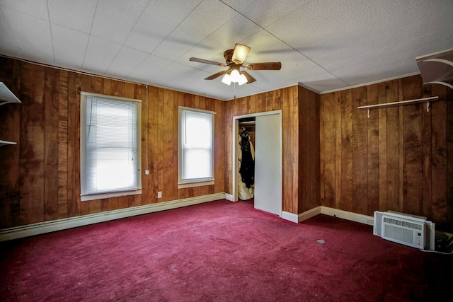 unfurnished bedroom featuring wooden walls, ceiling fan, a baseboard radiator, a closet, and an AC wall unit