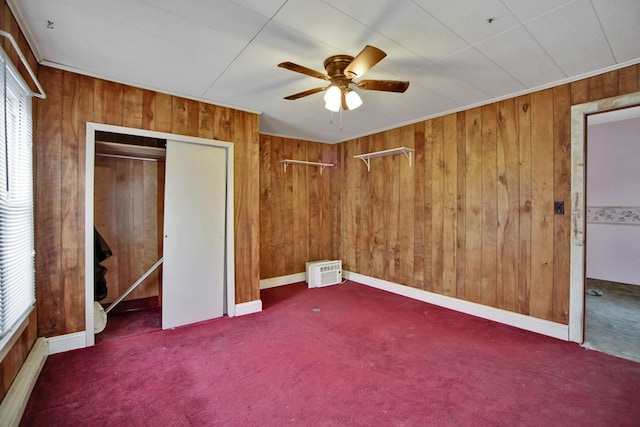 unfurnished bedroom featuring ceiling fan, a closet, wood walls, and dark colored carpet