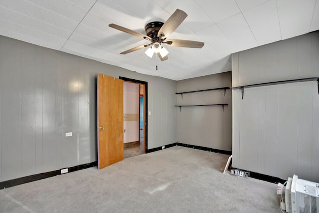 unfurnished bedroom with ceiling fan, light colored carpet, and wooden walls