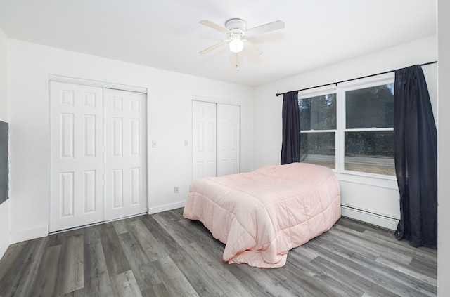bedroom with baseboards, wood finished floors, multiple closets, and a baseboard radiator