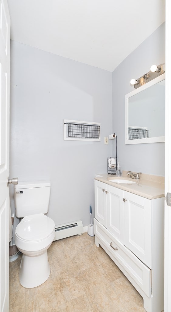 half bathroom featuring vanity, toilet, and baseboard heating