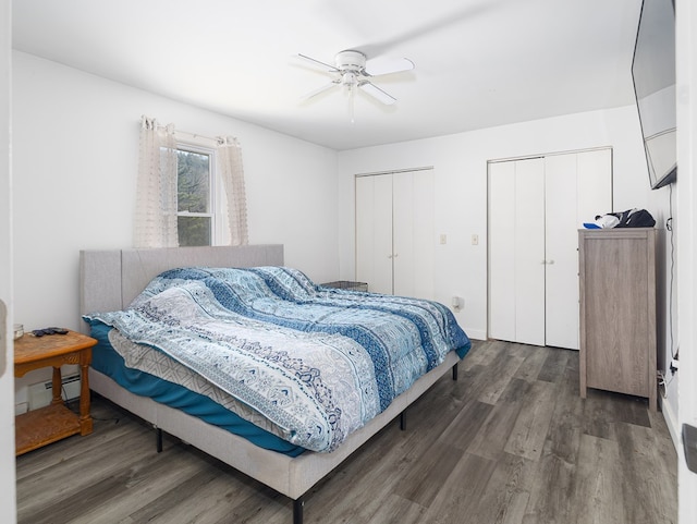 bedroom featuring baseboard heating, wood finished floors, two closets, and ceiling fan