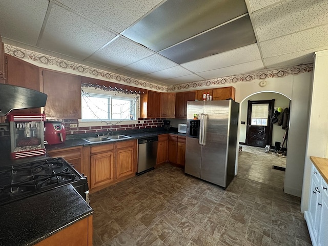 kitchen with brown cabinetry, dark countertops, extractor fan, stainless steel appliances, and a sink