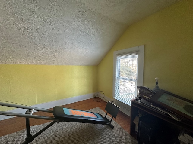 workout area featuring lofted ceiling, baseboards, a textured ceiling, and wood finished floors