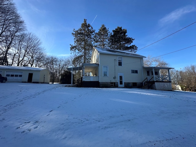 view of snow covered exterior featuring a garage, covered porch, and an outdoor structure