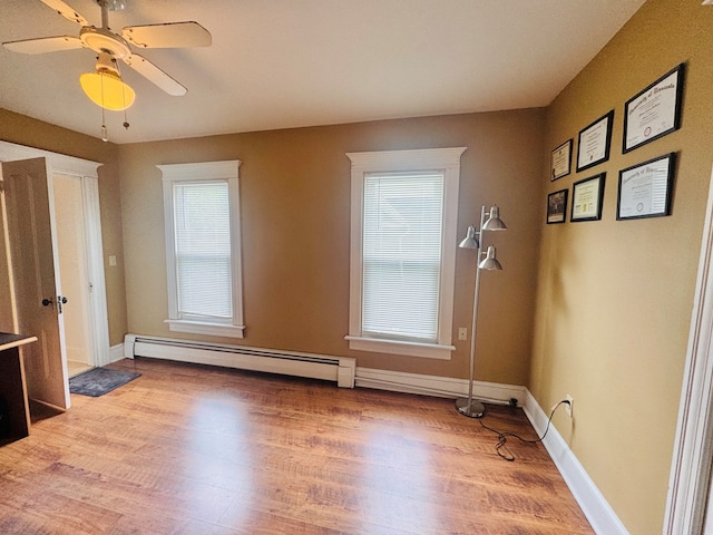 empty room featuring baseboard heating, plenty of natural light, light wood finished floors, and a ceiling fan