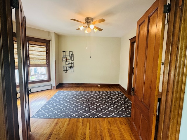 empty room featuring baseboards, a baseboard heating unit, light wood-style flooring, and ceiling fan