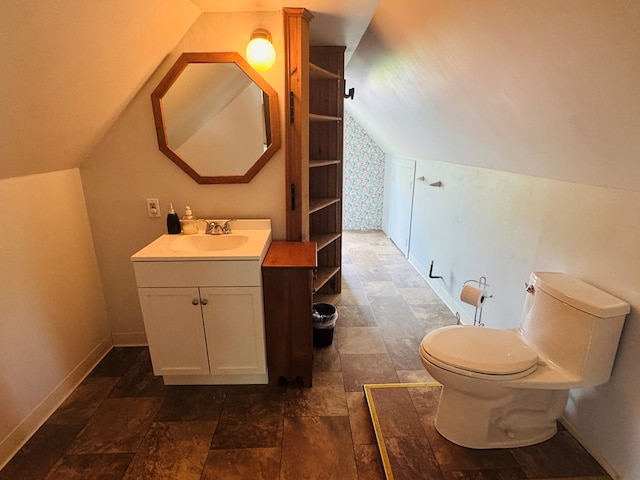 bathroom with lofted ceiling, stone finish flooring, baseboards, toilet, and vanity