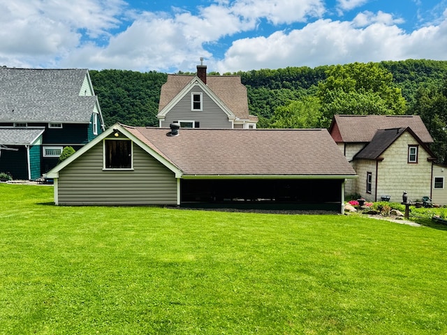 back of house with a lawn, a shingled roof, and a chimney