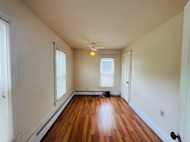 unfurnished room with a baseboard heating unit, healthy amount of natural light, wood finished floors, and baseboards