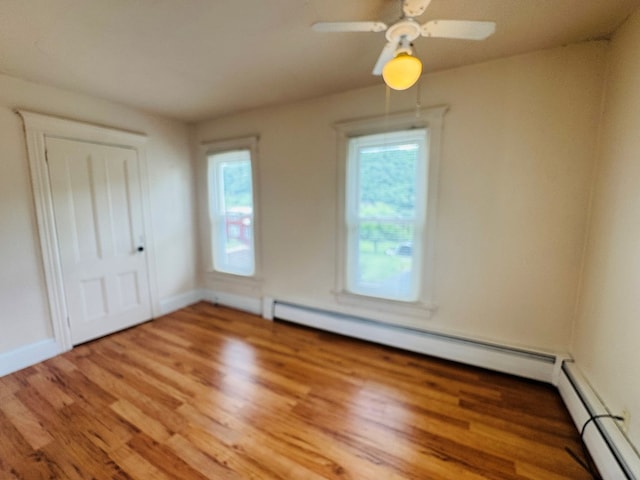 unfurnished room with plenty of natural light, wood finished floors, baseboards, and baseboard heating