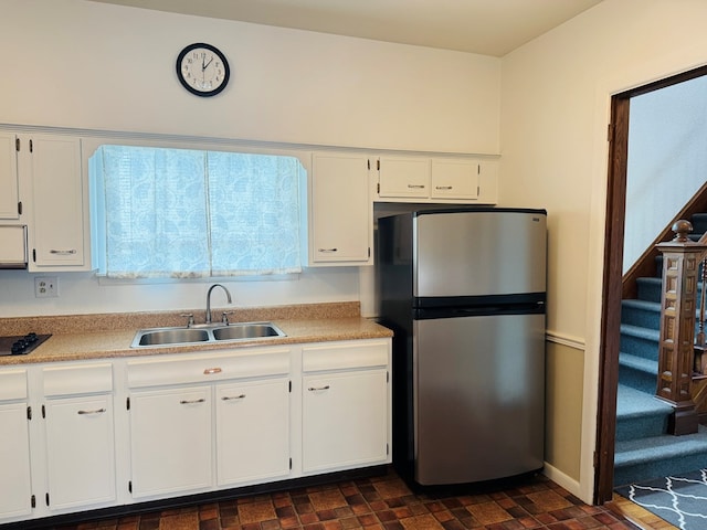 kitchen with freestanding refrigerator, a sink, white cabinetry, black electric stovetop, and light countertops