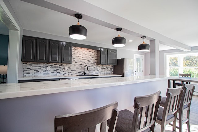 kitchen with light stone countertops, stainless steel fridge, backsplash, and sink