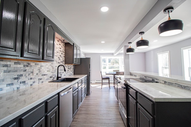 kitchen featuring appliances with stainless steel finishes, tasteful backsplash, sink, pendant lighting, and light hardwood / wood-style floors