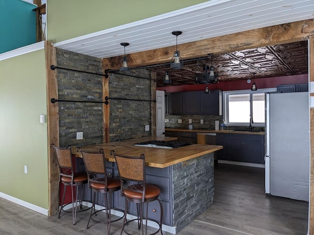 bar with wood counters, sink, decorative light fixtures, appliances with stainless steel finishes, and hardwood / wood-style flooring