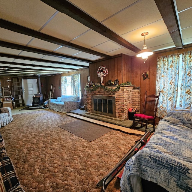 bedroom with carpet, wood walls, a wood stove, a fireplace, and beam ceiling