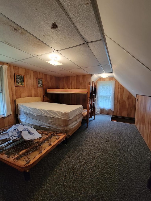 unfurnished bedroom featuring carpet flooring, a drop ceiling, wood walls, and vaulted ceiling