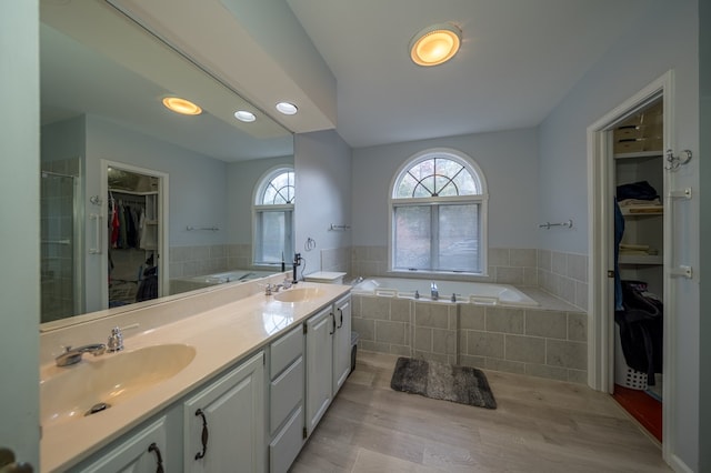 bathroom featuring a relaxing tiled tub, vanity, and hardwood / wood-style floors