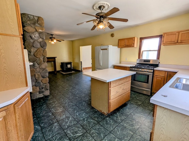 kitchen with stainless steel gas range, light countertops, freestanding refrigerator, a kitchen island, and a wood stove