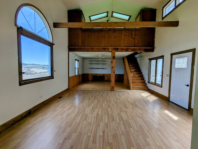 unfurnished living room featuring high vaulted ceiling, wood finished floors, wood walls, stairs, and baseboards