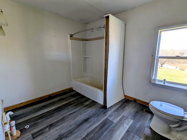 full bath featuring washtub / shower combination, toilet, plenty of natural light, and wood finished floors