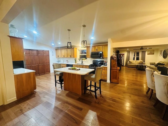 kitchen with open floor plan, light countertops, black appliances, a kitchen bar, and pendant lighting