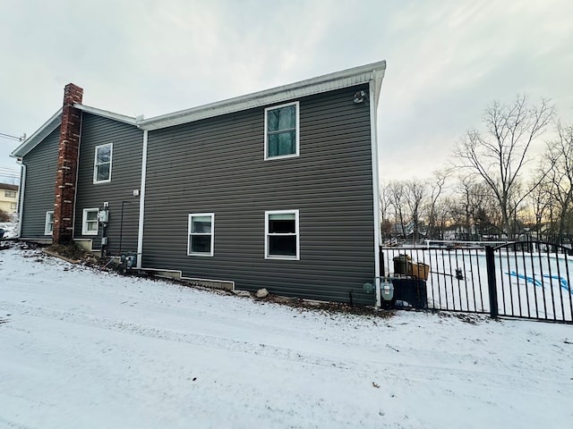 snow covered property featuring a chimney and fence