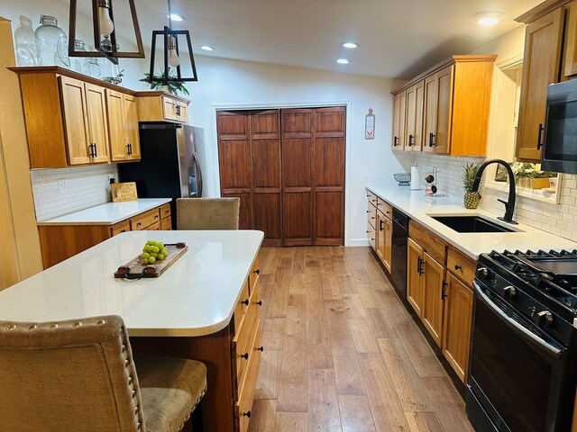 kitchen featuring decorative light fixtures, sink, backsplash, a kitchen island, and black appliances