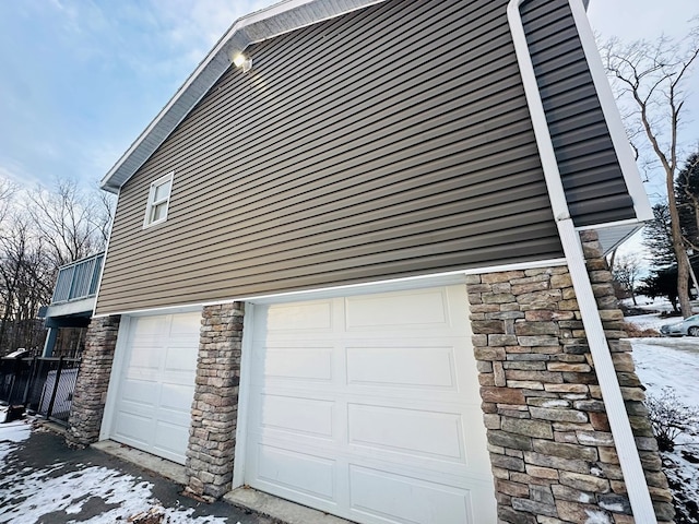 view of snowy exterior with stone siding and an attached garage