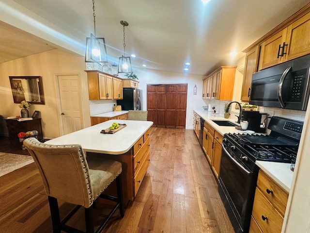 kitchen with a sink, light countertops, a center island, black appliances, and decorative light fixtures