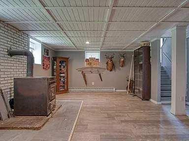 basement featuring a baseboard radiator, brick wall, wood finished floors, baseboards, and stairway