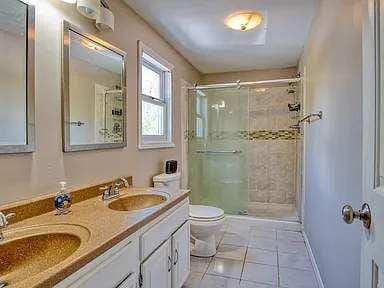 full bathroom with double vanity, a sink, toilet, and a shower stall