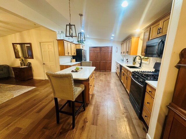 kitchen featuring a sink, hanging light fixtures, light countertops, a center island, and black appliances